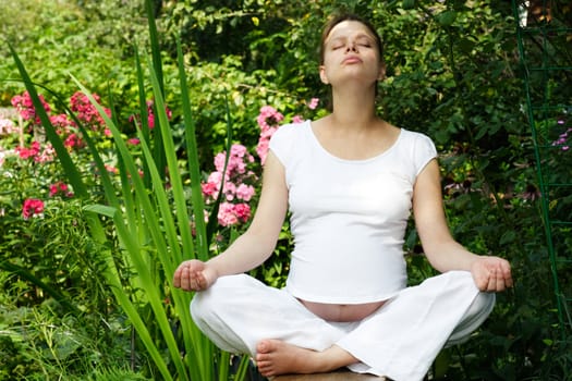 Young pregnant woman meditating at summer garden