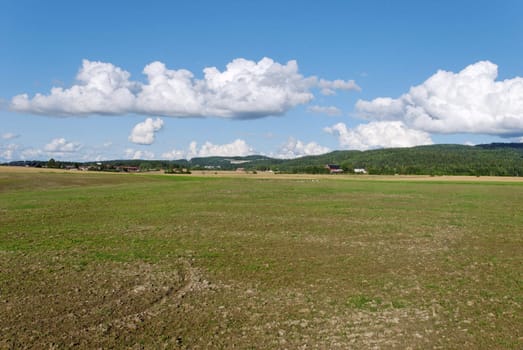 Field, prepared for the winter with farms in the distance and cloudscape above.
