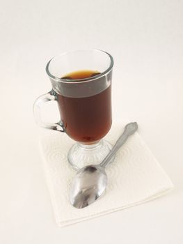 A glass of hot coffee and a silver tablespoon over a white background.