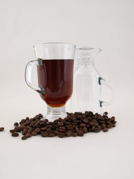 A hot glass of coffee sits next to an inverted glass amongst coffee beans. Isolated on a white background.