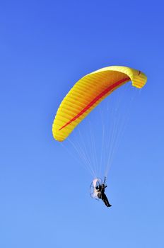 Man with a yellow paraglider flying in the sky