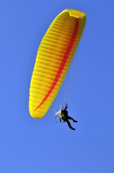 Man with a yellow paraglider flying in the sky