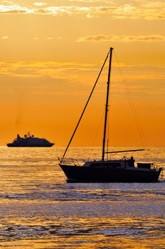 Two different kind of boats at sunset: a big yacht and a small sailboat