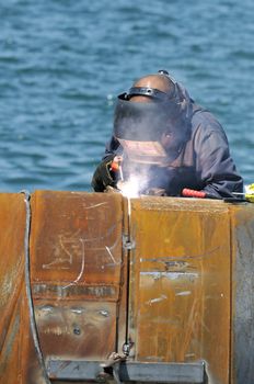 Worker welding two big pipes in a harbour