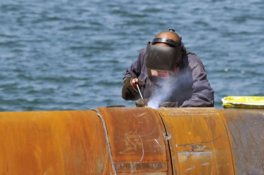 Worker welding two big pipes in a harbour