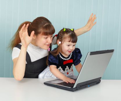 The girl and her mother are playing with the laptop sitting at the table