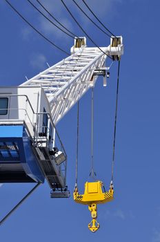 Blue and white crane with a yellow hook against a blue sky