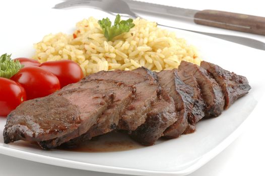 Sliced teryaki steak with rice pilaf and tomatoes.