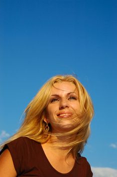 Smiling blond woman with fly-away hair against blue sky