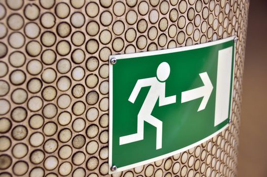 Green emergency exit sign on brown tiled column