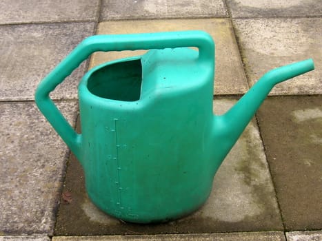 old plastic watering can standing on concrete slabs