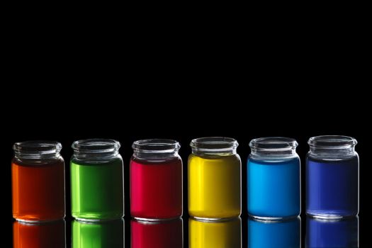 Line of glasses filled with colorful liquid isolated on black background with reflection.