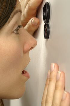 A surprised or frightened woman peering out through the peephole of her front door.
