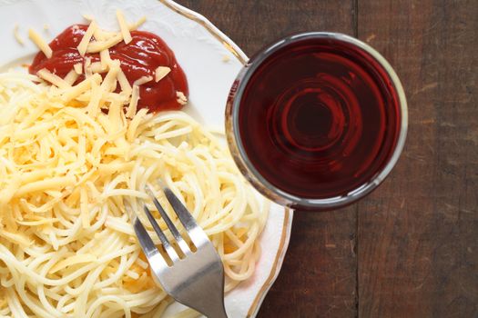 Plate with spaghetti and grated cheese near goblet of red wine on wooden background