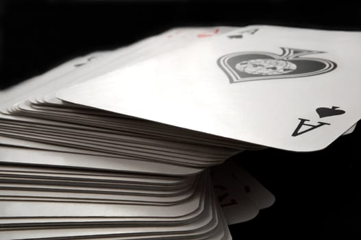 Close and low level focussing on the top card of a stack of playing cards with black background.