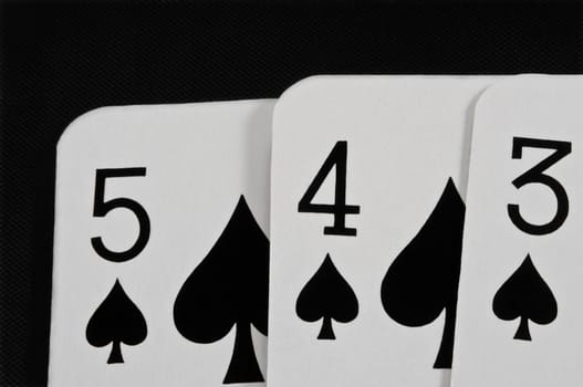 Close up on the top portion of three overlapping playing cards arranged over black.