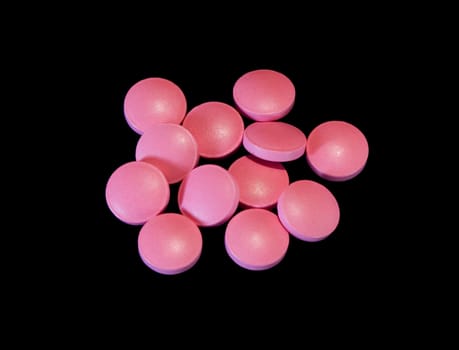 Pile of pink pills isolated on black background