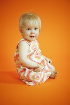 Small girl sitting on the orange background in studio