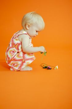 Young baby girl picking up flowers from the floor
