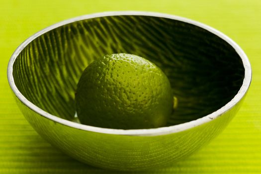 One lime on the small metal bowl over green background