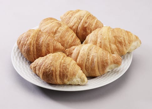 A few fresh hot croissant display on a round white plate.