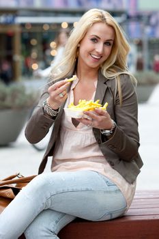 Pretty young girl in the city eating fries with mayonaise