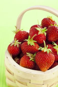 Wooden basket filled with strawberries over green background