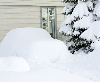 Car parked outside a house, completely covered with snow.