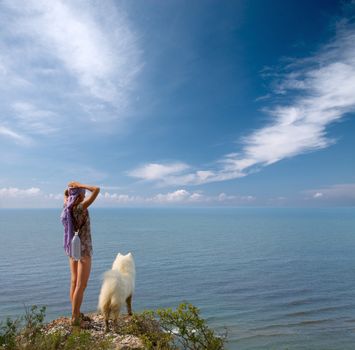 Girl with bottle and samoyed dog standing on precipice above sea