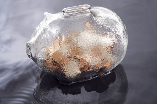a glass piggy bank with coins  feflecting on a water base background