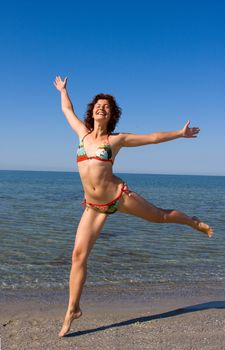 Happy smiling girl in bikini dancing at sea coast