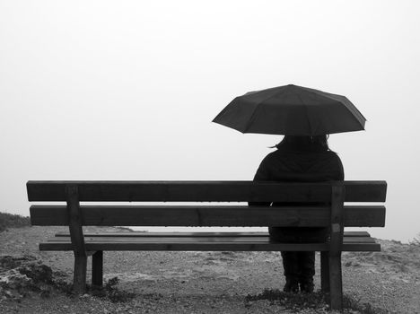 Woman with an umbrella sitting on a bench at a cliff edge