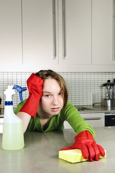 Tired girl doing kitchen cleaning chores with rubber gloves