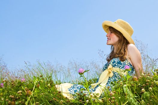 Young teenage girl sitting on summer meadow in straw hat