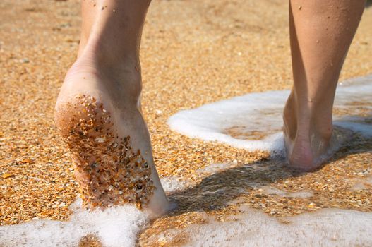 barefoot feet walking in surf on sand coast