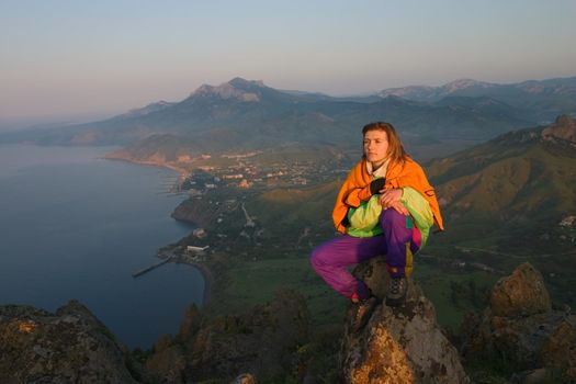 Girl siting on a cliff under the sea and looking on sunrise