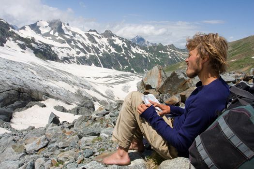 barefoot alpinist sitting on rock and looking to map in wild mountains