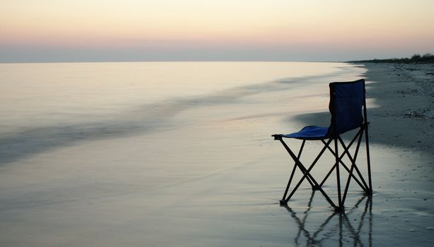 Folding chair standing on a wet sand on a seaside 