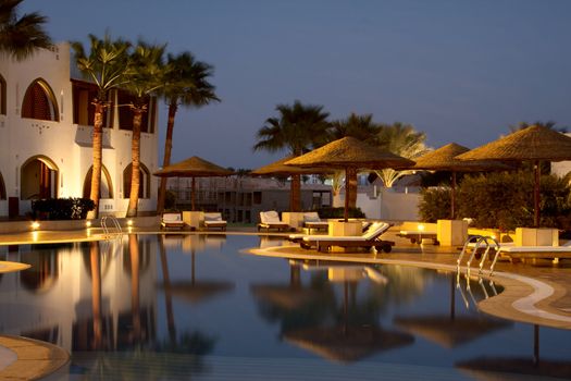 evening illumination in tropical hotel. swimming pool and sunshades