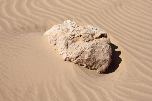 Sand in desert with wind texture and big stone