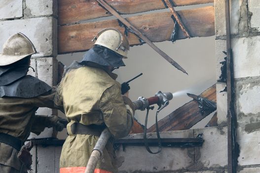 Firefighter with firehose spraying water in window of flaming house