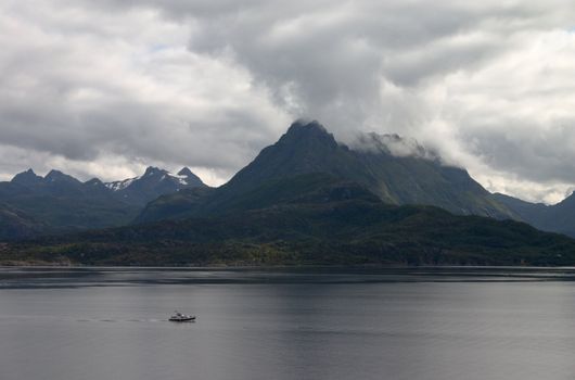 sombre seaside landscape with boat and mountains under clouds in north norway