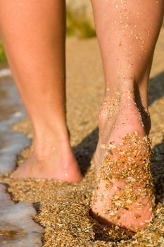 Girl's barefoot feet on beach in sea surf
