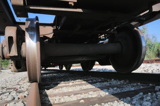 looking up at a rusty freight train car with wheels polished to a shiny finish by the railroad tracks underneath