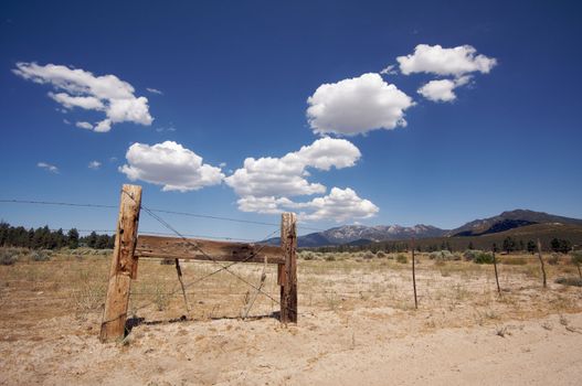 Puffy Storm Clouds Forming Over Field and Aged Fence on a blue sky.