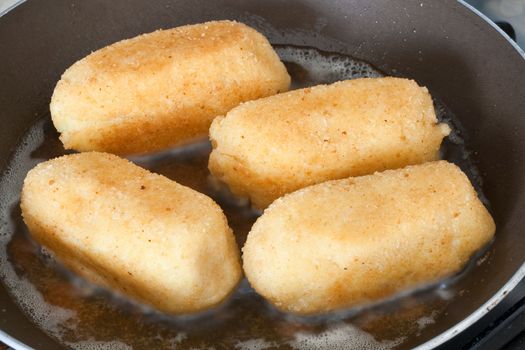 closeup of four potato croquettes cooked on a frying pan