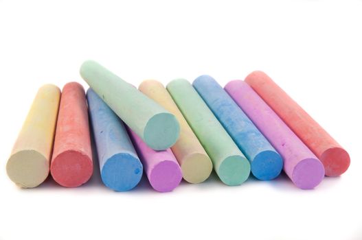 Close and low level capturing a selection of coloured art chalk sticks arranged over white.