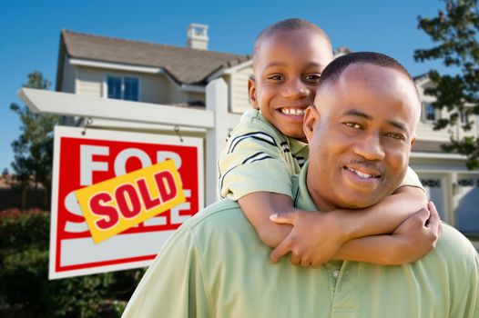 Happy African American Father and Son in Front of New Home and Real Estate Sign.