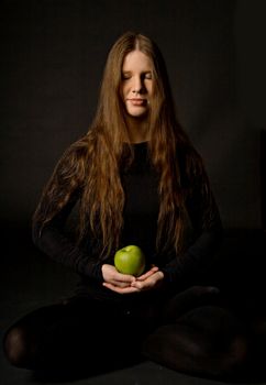 The portrait of a woman with a green apple in her hands, black background