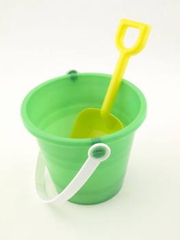 a yellow plastic shovel inside of a green bucket isolated on a white background